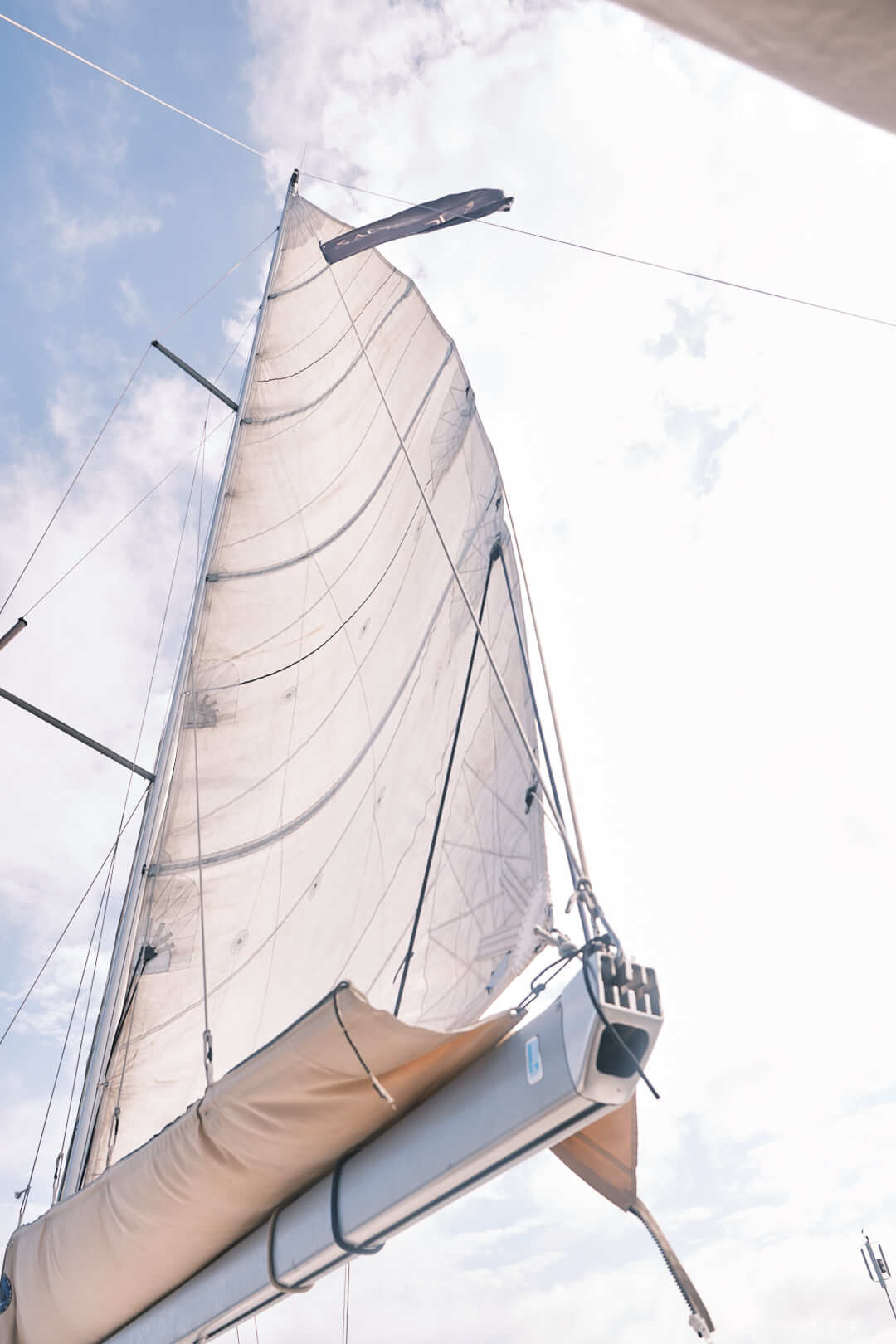 La vela mayor de un velero está completamente izada con un cielo nublado como telón de fondo, creando el escenario perfecto para el Curso de Navegación: Aparejado y Trimado de Velas con La Marina de València.