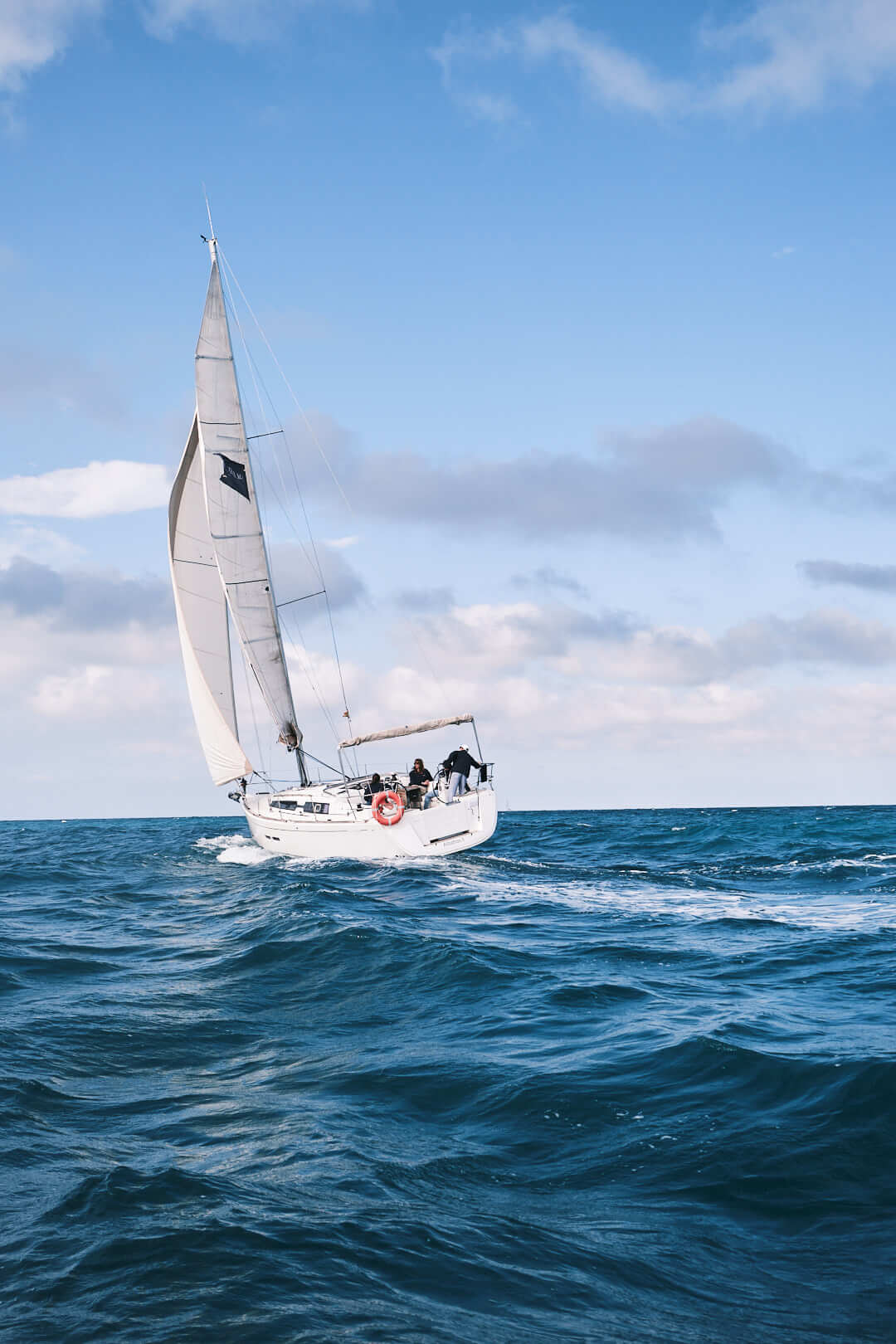 Un velero elevado maniobra en un mar azul claro bajo un cielo parcialmente nublado cerca de La Marina de València, mostrando las habilidades del Curso de Navegación: Aparejado y Trimado de Velas.