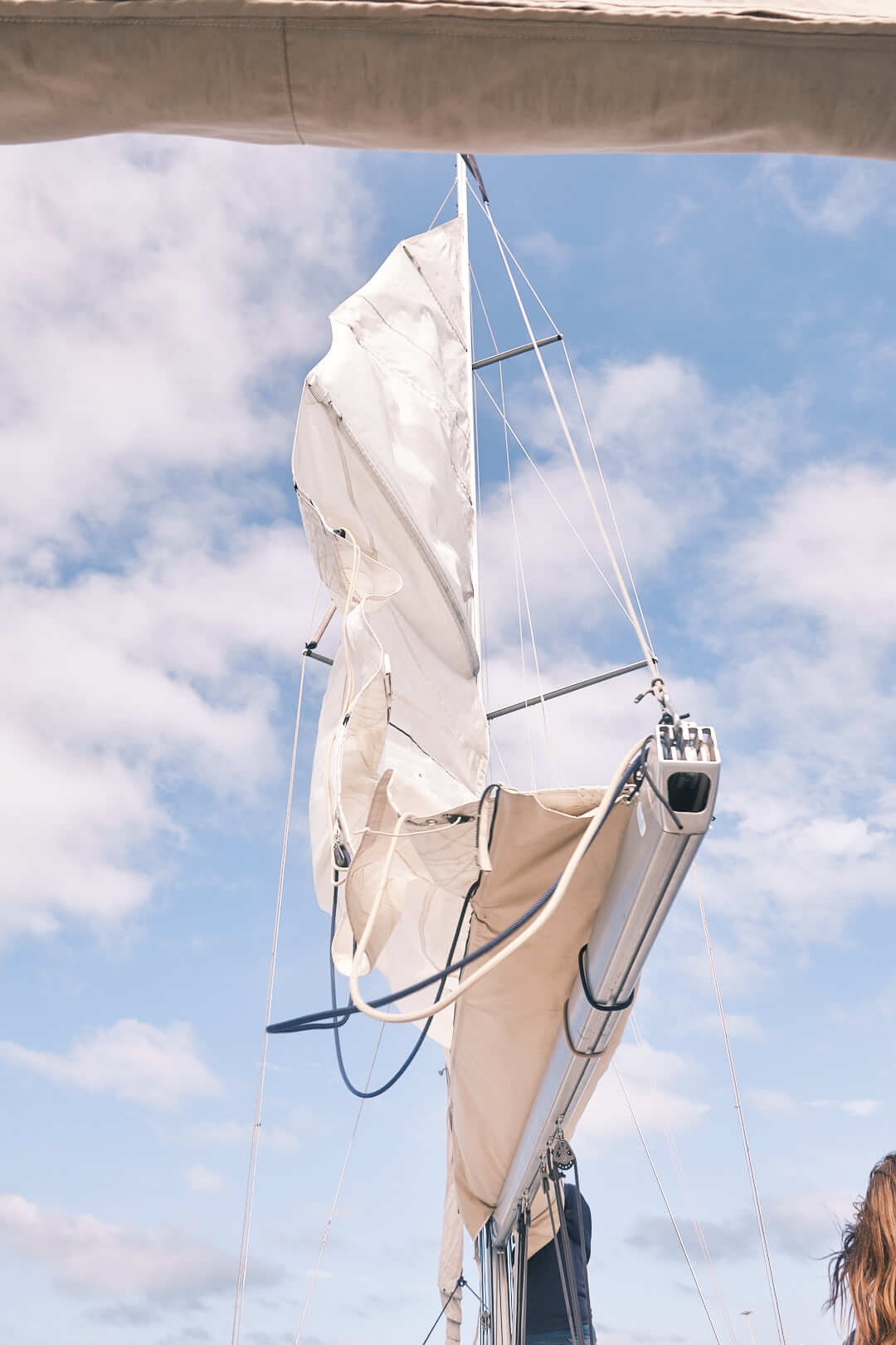 El mástil de un velero con la vela parcialmente izada se alza orgulloso contra un cielo azul con nubes en La Marina de València, perfecto para realizar el "Curso de Navegación: Meteorología" de DÍASábados.