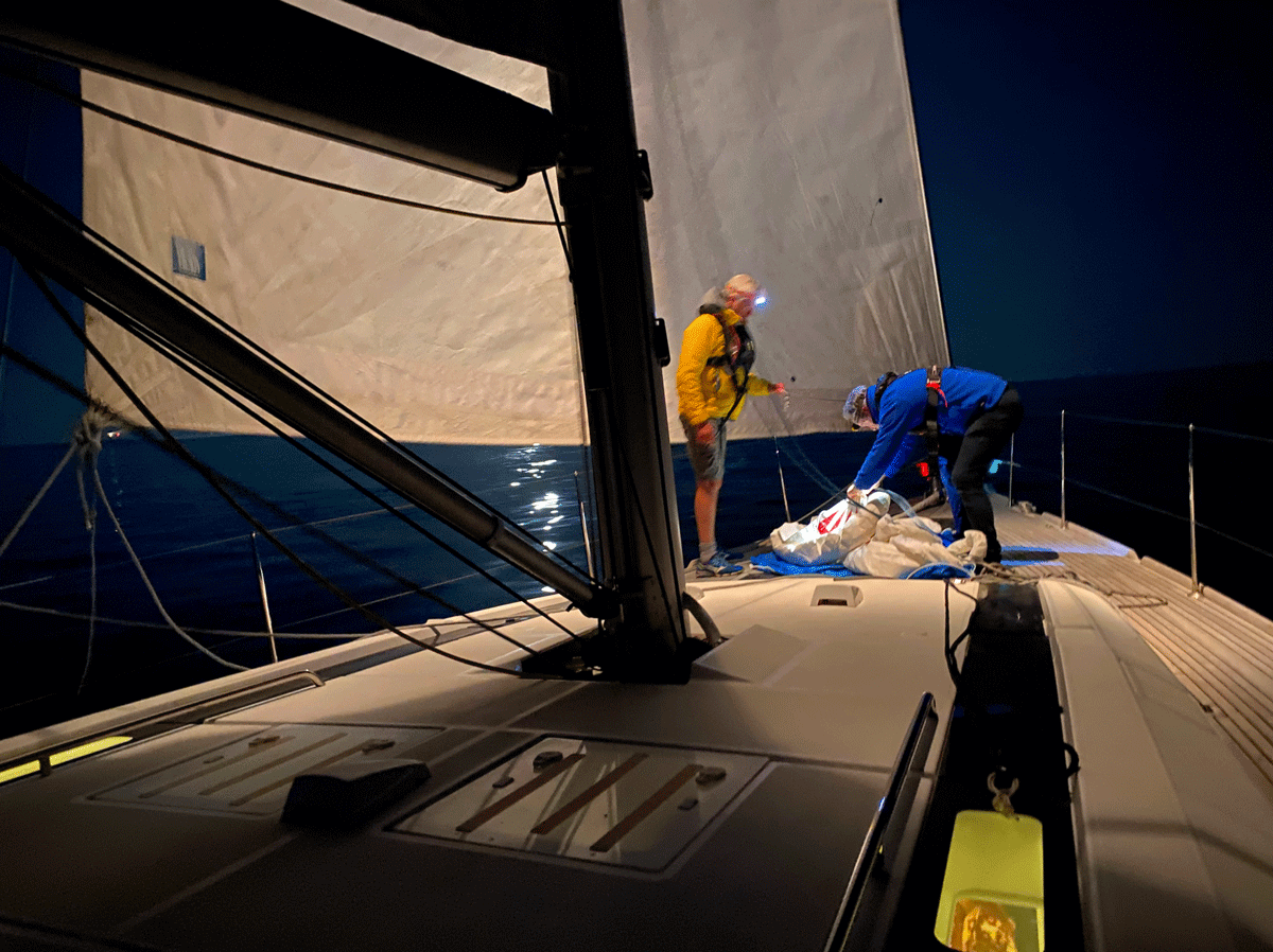 Bajo el cielo oscuro, Oscar García Flores y su tripulación trabajan diligentemente en la cubierta de un velero, ajustando la vela y los cabos. Este Curso de Navegación: Nocturna se desarrolla en La Marina de València, donde cada noche se perfecciona el conocimiento marítimo.